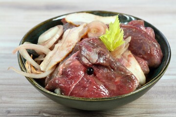 Fresh deer meat  marinated in red wine with bakon, onion, garlic and juniper berries. Bowl with pieces of deer meat on  wooden table.