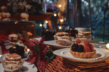 Mesa de postres. Pequeña tarta de frutos rojos sobre canasta con fondo de luces y adornos navideños