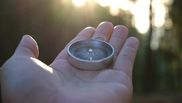 Compass in hand on natural pine forest background. hand holding compass in forest landscape. Young traveler searching direction with compass in summer mountains.