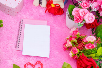 Obraz na płótnie Canvas White blank notebook paper on the top of a pink notebook surrounded by valentine themed decorations