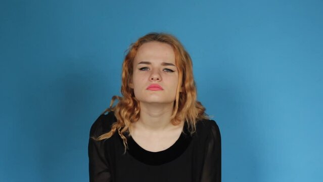 A young shocked surprised woman standing isolated on a blue background looking at the camera.