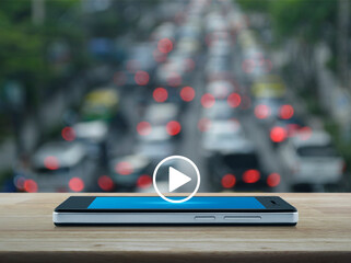 Play button flat icon on modern smart mobile phone screen on wooden table over blur of rush hour with cars and road in city, Business music online concept