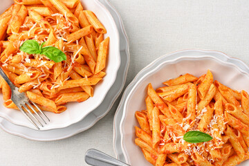 Close-up of a plate of All'Arrabbiata penne pasta with basil leaves on a linen tablecloth. Top view.