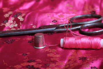 Spool of Pink Thread and Thimble on Vintage Pink Satin Fabric