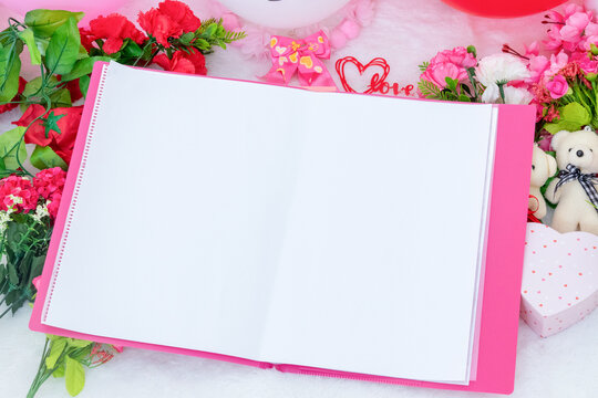 White blank A4 paper on the to of a pink file folder surrounded by valentine themed decorations