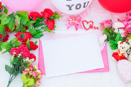 White blank A4 paper on the to of a pink envelope surrounded by valentine themed decorations