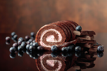 Chocolate roll cake with blueberries and a broken black chocolate bar.
