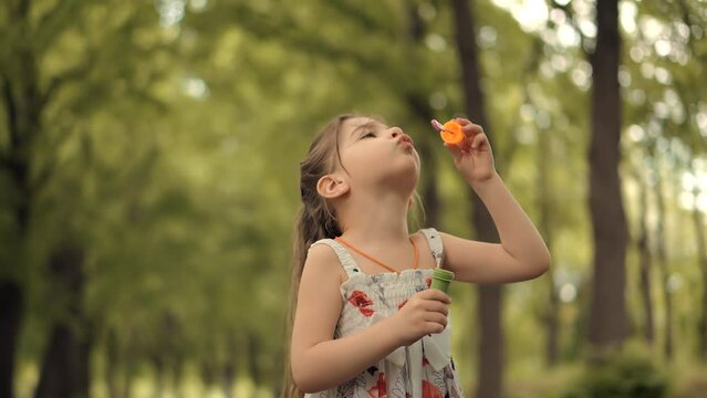 preschool girl blowing soap bubbles and playing outdoors