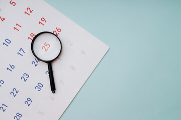 Black magnifying glass and calendar on blue background, top view