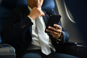 Cropped shot of businessman passenger checking news on smart phone, using wireless connection on board during flight