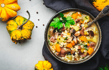 Winter comfort food. Warming high-calorie soup with pumpkin, mushrooms, potato, beef and barley. Gray table background, top view, copy space