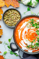 Pumpkin soup with seeds, cream and green pea sprouts. Winter or autumn healthy slow food. Soup bowl on gray table background. Top view