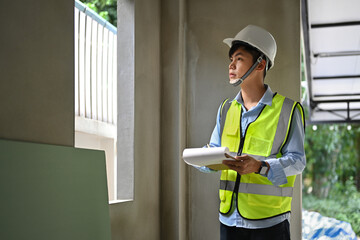 Image of engineer man looking at clipping board and checking building construction progress, working at construction site