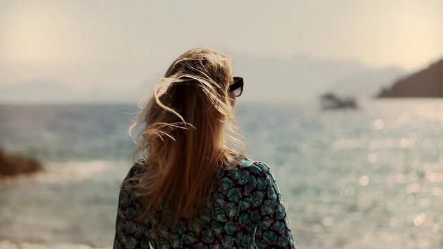woman walks along ocean and hair flowing in sea breeze	