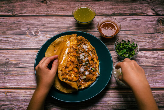 Hands of a person preparing a gringa pastor a la diabla accompanied by sauces and other condiments on a wooden table. Gringa, typical Mexican dish.
