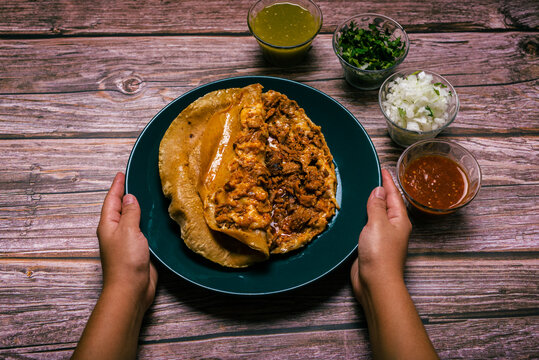 Hands of a person preparing a gringa pastor a la diabla accompanied by sauces and other condiments on a wooden table. Gringa, typical Mexican dish.