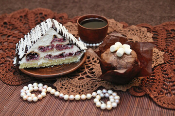 A beautiful still life - a cake, a cup of tea, beads with pearls, cupcakes, on lace napkins.