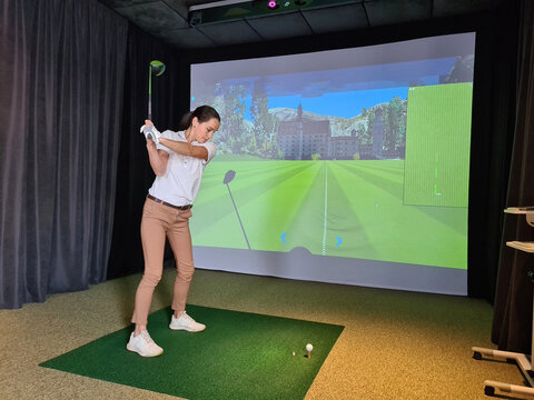 Girl playing golf on screen and golf simulator