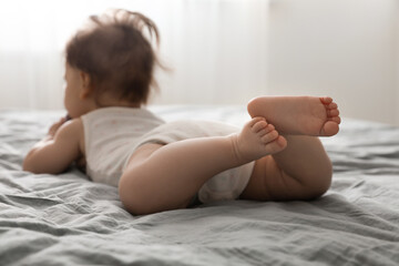 Little baby lying on bed indoors, focus on legs