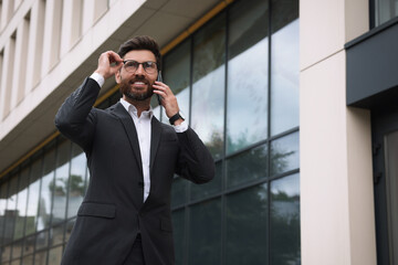 Handsome businessman talking on smartphone while walking outdoors, space for text