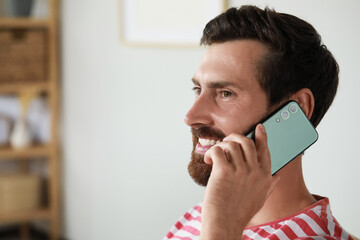 Handsome man talking on phone at home, space for text