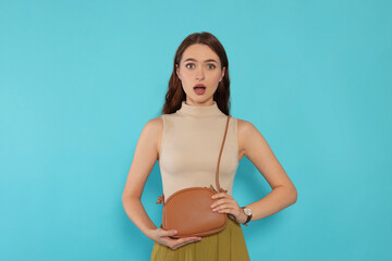 Emotional young woman in fashionable outfit with stylish bag on light blue background