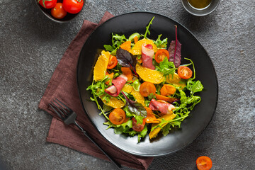 Fresh salad with arugula, cherry tomatoes, orange slices and smoked duck slices on a black plate on...
