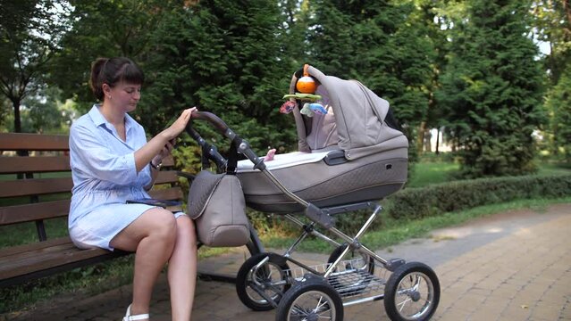 Zoom in camera. A woman is sitting with a stroller in a park. She's talking on the phone. 4K Slow Mo