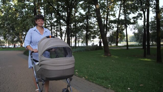Mom with a baby in a stroller slowly walks along the path in the park. 4K Slow Mo