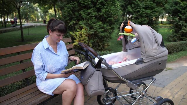 Mom reads a book on a bench. Near the woman lies a baby in a stroller. 4K Slow Mo