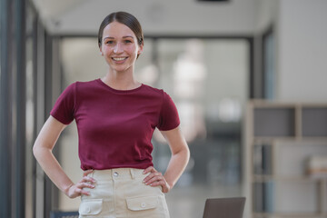 A casual young businesswoman standing with her hands on her hips and smiling at the camera.