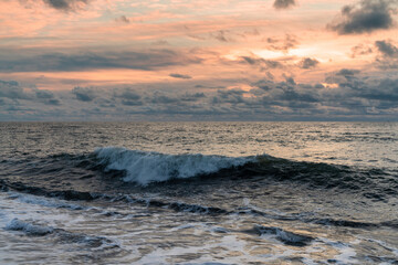 large wave breaking and rolling to shore under a stormy sunset sky