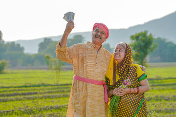 Indian farmer couple standing at agriculture field and showing rupees