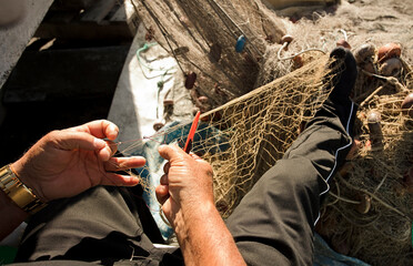 fishing net in the hands of fisherman, with needle and thread, grabs net with toes