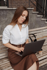 Young business woman sitting on a bench with a laptop of the modern office building background 