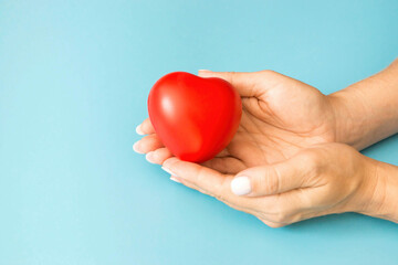 in female hands a heart toy on a blue background, copyspace on the left. concept insurance, female heart health, organ donation, bone marrow transplantation, prevention of heart disease