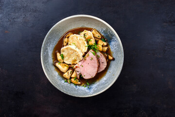 Traditioneller deutscher Schweinebraten mit Semmelkn&ouml;del und Baby Kr&auml;uterseitlinge in dunkler Biersauce serviert als Draufsicht in einer Nordic Design Schale mit Textfreiraum