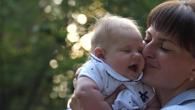Portrait of happy mother and newborn baby. Smiling woman raises her infant daughter and kissing her with love. 4K Slow Mo