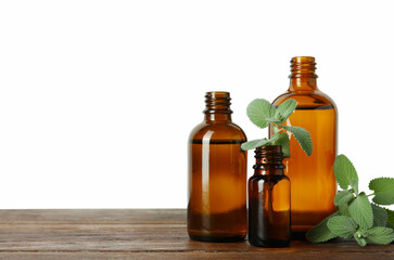 Bottles of essential oil and mint on wooden table against white background