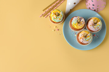 Cute sweet unicorn cupcakes and party items on yellow background, top view. Space for text