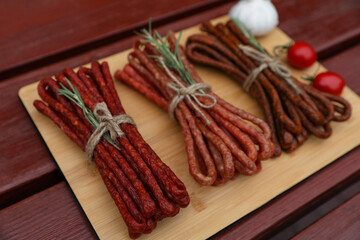 Bundles of delicious kabanosy with rosemary, tomatoes and garlic on wooden table
