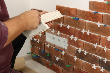 Professional builder applying cement onto decorative brick near wall, closeup. Tiles installation process