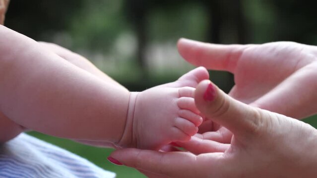 Close-up female hands stroking baby's feet. Mother and infant girl bonding and having fun outdoors in nature. 4K Slow Mo