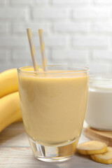 Glass of tasty banana smoothie with straws and ingredients on white wooden table