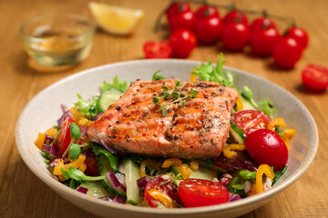Bowl with tasty salmon and mixed vegetables on wooden table, closeup