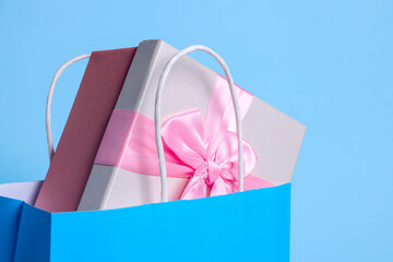 Bright paper shopping bag with gift box on light blue background, closeup
