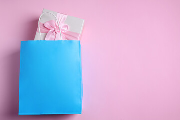 Light blue paper shopping bag with gift box on pink background, top view. Space for text