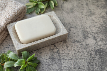 Fototapeta na wymiar Dish with soap bar, terry towel and green plants on light grey textured table. Space for text