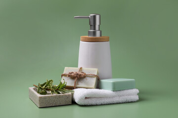 Obraz na płótnie Canvas Soap bars, bottle dispenser and towel on green background