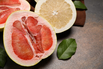 Fresh cut pomelo fruits with green leaves on dark table, closeup. Space for text